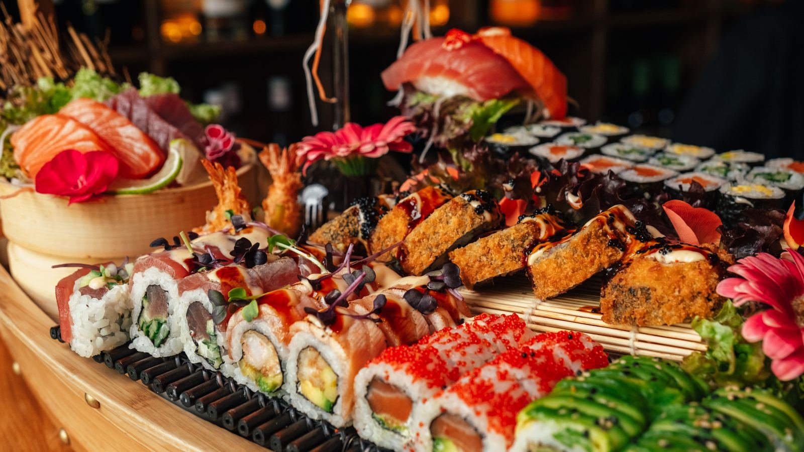 Reich belegtes Sushi-Boot mit Sashimi, Maki, Nigiri und Tempura auf dunklem Holztisch