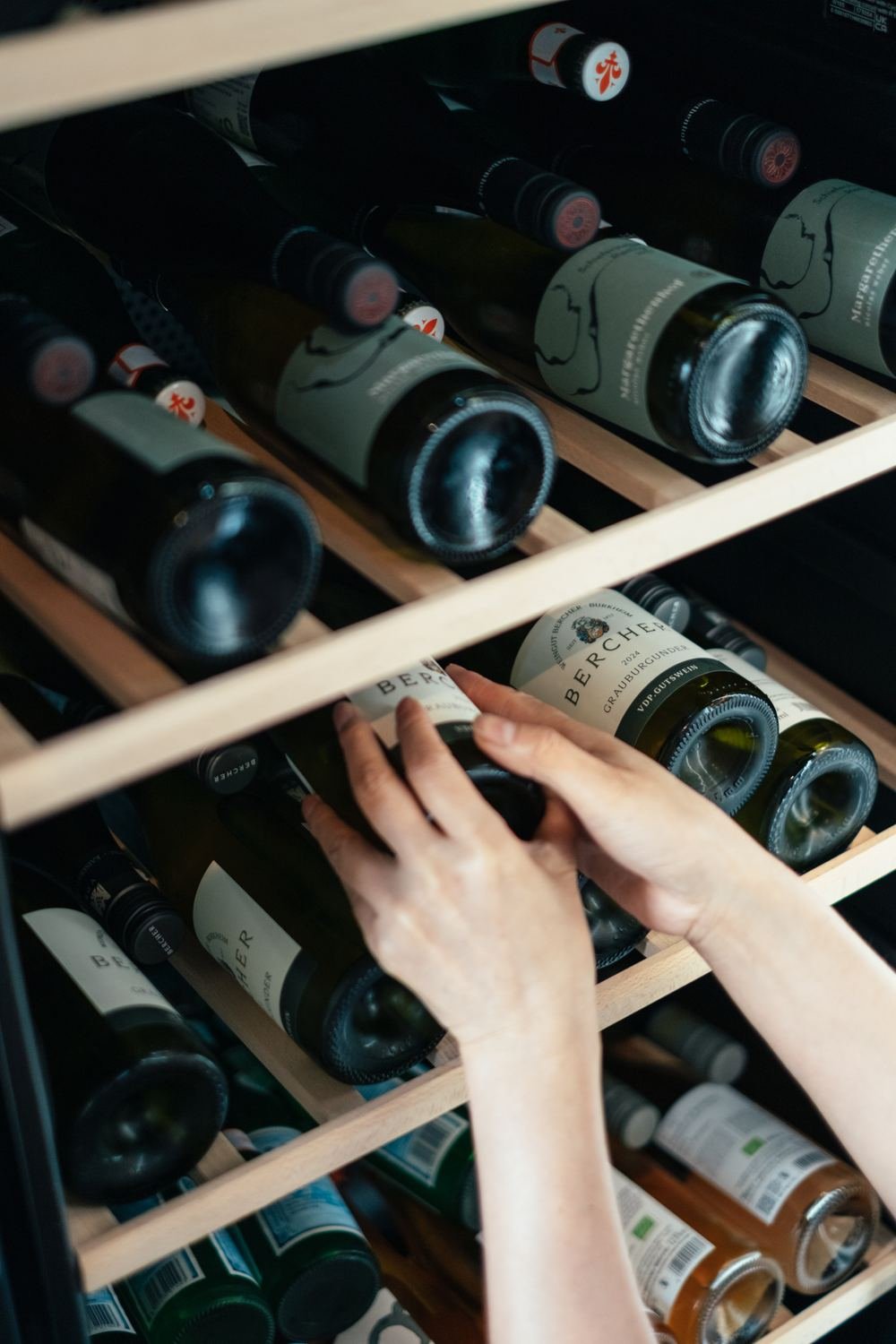Hand greift nach einer Weinflasche im gut sortierten Weinschrank